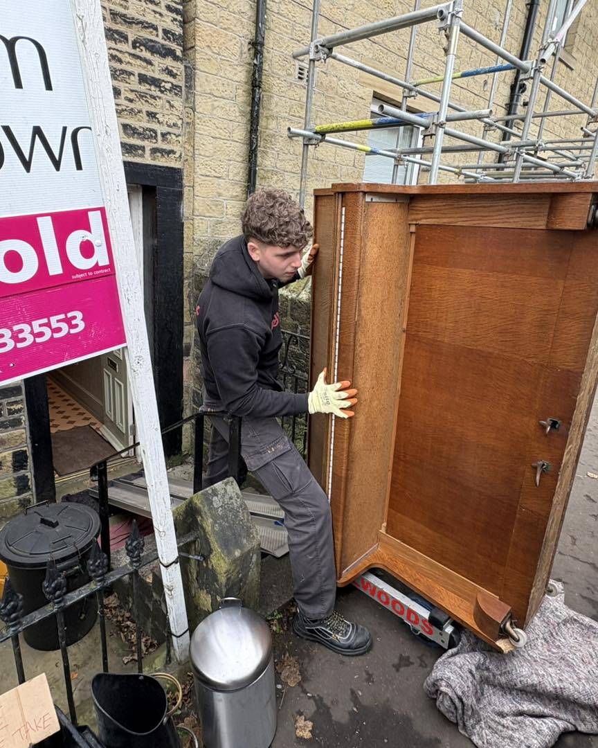 Oak upright piano being carefully moved past a Sold sign